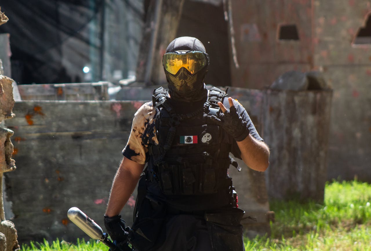 Home Armed paintball player with helmet and tactical gear in dynamic outdoor setting.