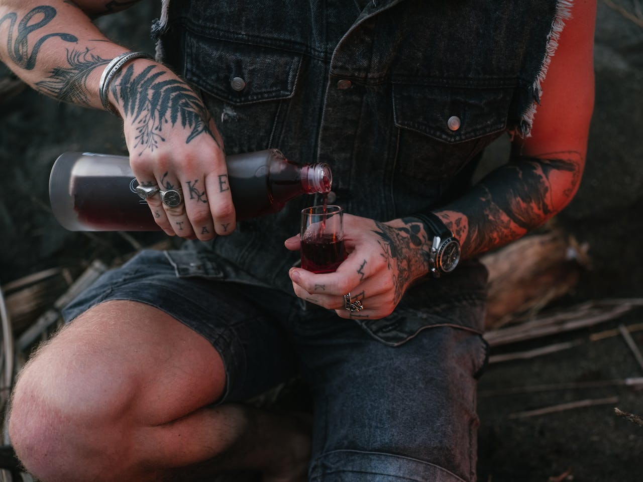 Close-up of tattooed hands holding a glass of red wine outdoors. A modern lifestyle scene.